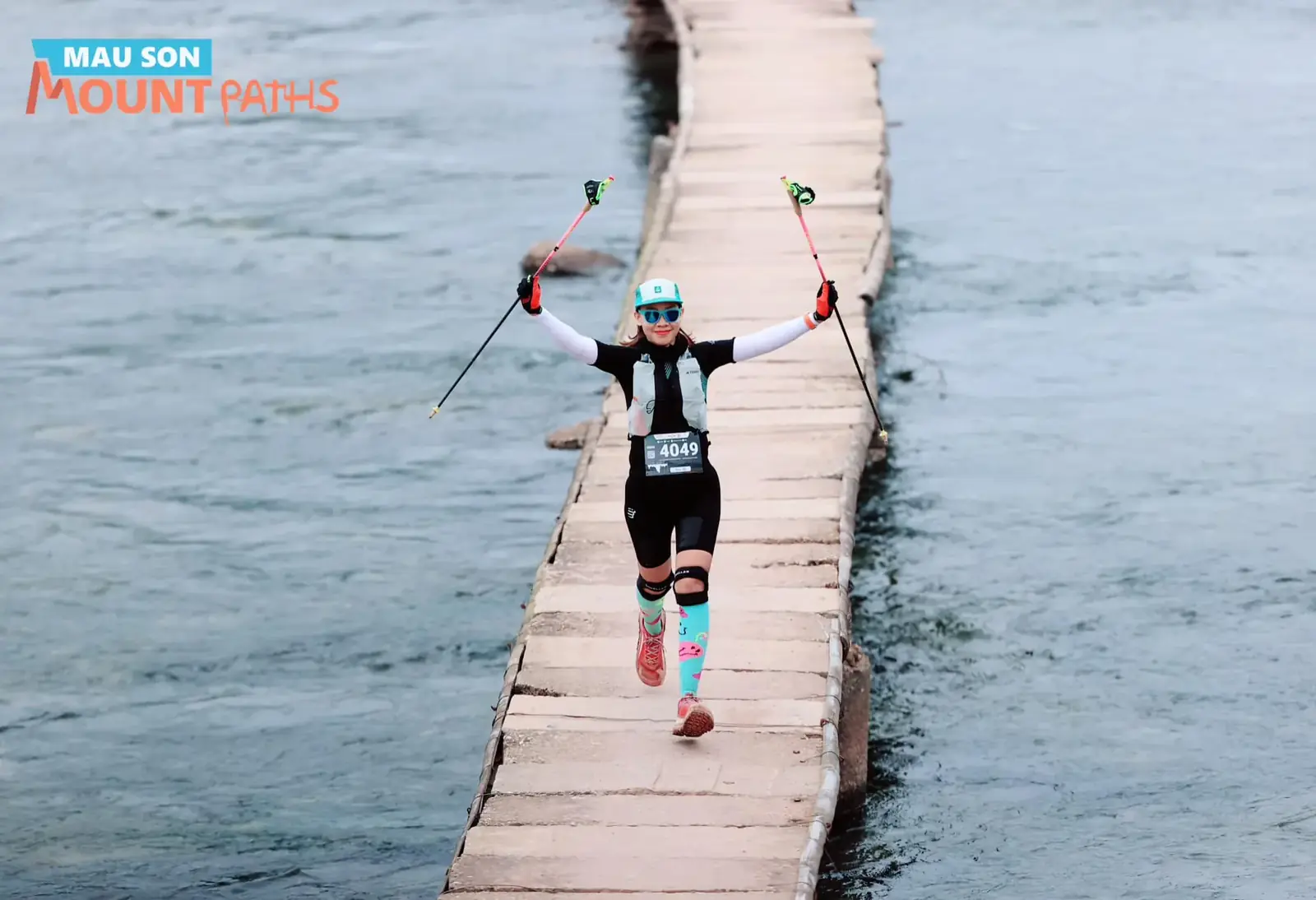 Trail runner raising her poles while crossing a wooden bridge over a lake at Mau Son Mountain Paths